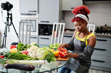 African american woman filming her blog broadcast about healthy food at home kitchen. She cuts red pepper.