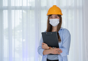 Female Engineer wear face mask with safety yellow helmet standing inside building check the correctness of the construction.