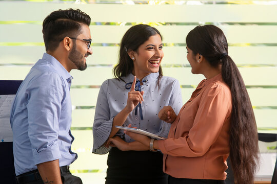 YOUNG WOMAN HAPPILY TALKING TO HER COLLEAGUES IN OFFICE	
