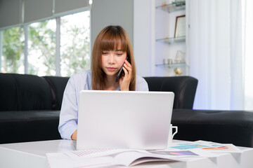 Naklejka premium Work from Home, Beautiful young woman working on laptop computer while sitting at the living room, Online meeting from home and Phone calls with customers.