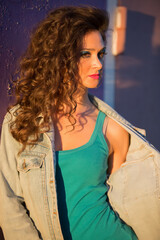 Beautiful young woman in a denim jacket on the background of a peeled purple wall. Girl with bright makeup in the style of the eighties on the street.