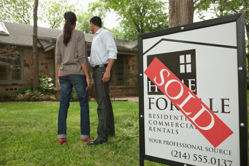 Couple standing in yard with sold sign