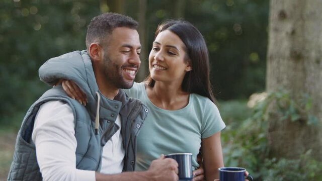 Romantic couple camping in countryside sitting by bonfire in fire bowl with hot drinks - shot in slow motion