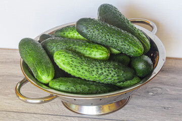Fresh cucumbers in a colander over wooden background. Fresh produce from the Farmers Market.
