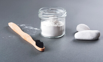 Zero waste concept for teeth cleaning. The bamboo toothbrush with the toothpowder and two white stones in the glass on the grey background.