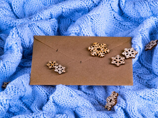 Beautiful brown paper envelope on the cute pale blue wool knitted background with the handmade wooden snowflakes.