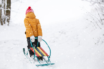 A child pulls a metal sled uphill in winter.