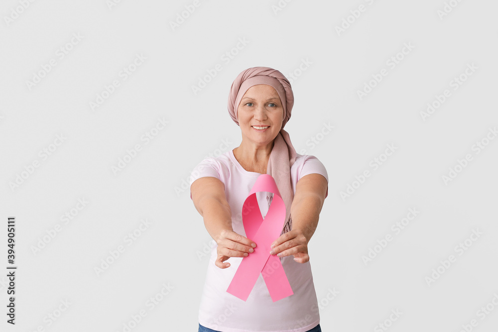 Wall mural mature woman after chemotherapy with pink ribbon on light background. breast cancer awareness