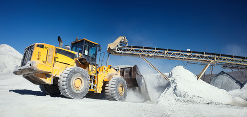 Front end loader near the stone crushing equipment at the limestone quarry against the blue sky, panoramic image. Mining industry.