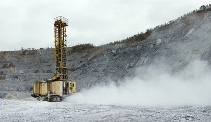Drilling machine in a limestone quarry in a cloud of dust, panorama.