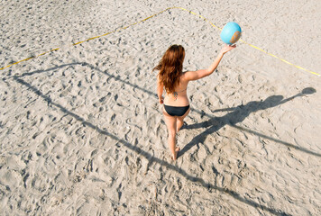 Back view of young volleyball player bouncing ball while walking on the sand