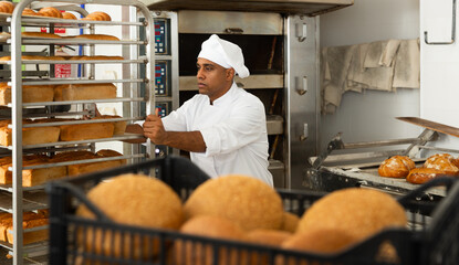 Man baker transporting a cart with bread in the bakery