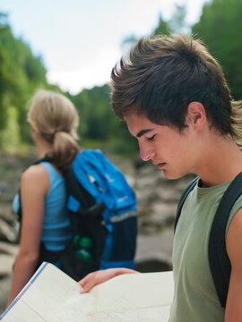 Young couple tramping in the wilderness and young man checking his map for directions