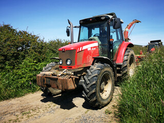 A tractor in a country lane with high hedges around the edge of a field. Rural farming concept during harvest season - UK
