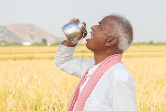 Thirsty Indian farmer drinking water from steel tumbler or Chambu on hot sunny day at agriculture field