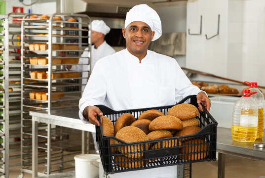 positive male baker with sesame bread in black box in kitchen