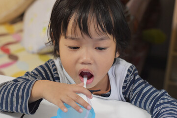 Child drinking from a glass with a straw but look at mobile phone