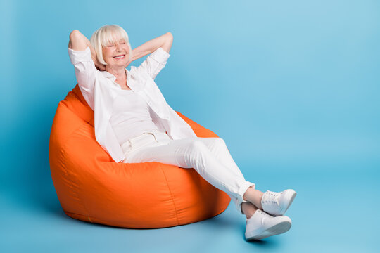 Full length body size photo of smiling granny resting relaxing closed eyes sitting in beanbag isolated on vibrant blue color background