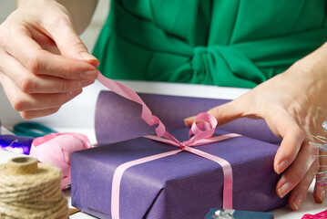 Female hands holding a small gift box wrapped in packing paper. To give and receive gifts from...