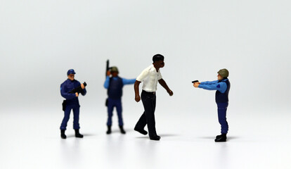 Fototapeta premium A police miniature blocking a walking black miniature man and pointing a gun at him. The concept of racial discrimination through abuse of public power. 