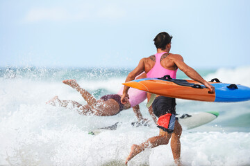 Team of male surf lifeguards training and running into sea holding ocean surf skis
