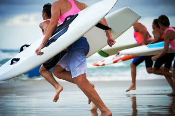 Close up of team of male surf lifeguards training and running into sea holding ocean surf skis