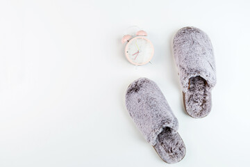 Flat lay with Soft fluffy slippers gray color and pink alarm clock isolated on white background. top view, overhead, mockup, template, copy space. Time for rest