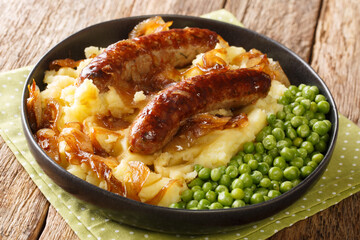 Tasty Bangers and Mash made of sausages served with mashed potatoes, green peas and onion gravy close-up in a plate on the table. Horizontal