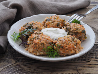 Meatballs with meat and rice, sour cream sauce, fresh herbs in a plate, fork and napkin on a wooden table. Recipe for a light, hearty and delicious meal for lunch, closeup
