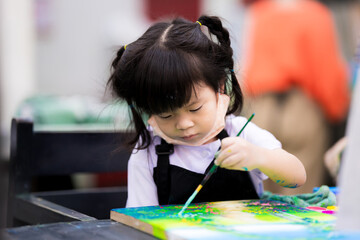 Cute girl is coloring on a canvas. Children work on watercolor art. Child wear black aprons to...