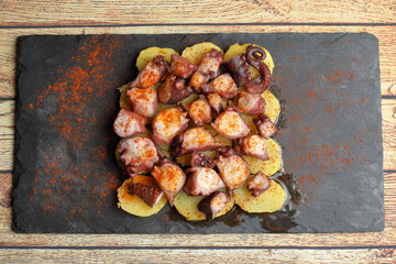 Galician octopus portion (pulpo a feira) on slate plate on rustic wooden table