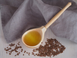 Flaxseed oil in a wooden spoon and linseeds with a linen napkin on a white wooden background, top view. Natural healthy oleum lini with omega and vitamins for vegetarian diets