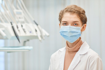 Portrait of young female dentist in protective mask looking at camera standing at dental clinic