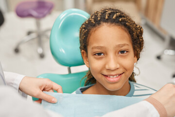 Portrait of African little girl smiling at camera while sitting on chair she visiting dentist