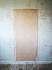 Empty room during renovation with unpainted walls with a blocked up doorway and bare floorboards - UK.