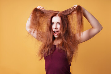 frustrated young woman pulling and tearing her long red hair on a bad hair day