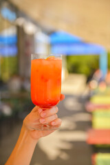 Hand with alcohol cocktail over blurred background, selective focus. Delicious refreshing alcohol beverage in restaurant