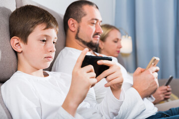 Modern young family sitting with smartphones in home interior