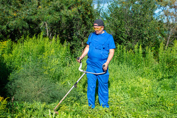 Man in a blue jumpsuit mowing the grass with a trimmer.