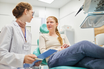Obraz premium Female patient sitting on dental chair and discussing medical procedure together with dentist at clinic