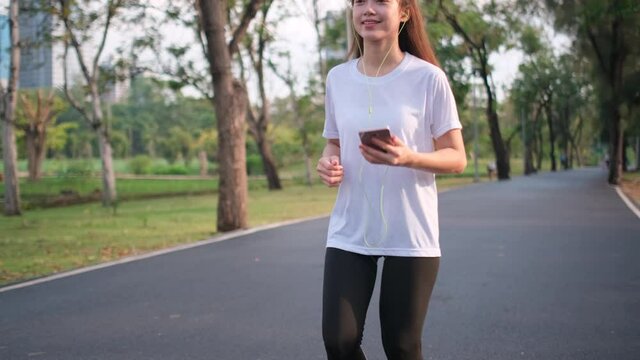 Asian sport woman is running in place double time in green park and also listen music from mobile phone. Concept of exercise and practice of healthy activity support good health lifestyle.