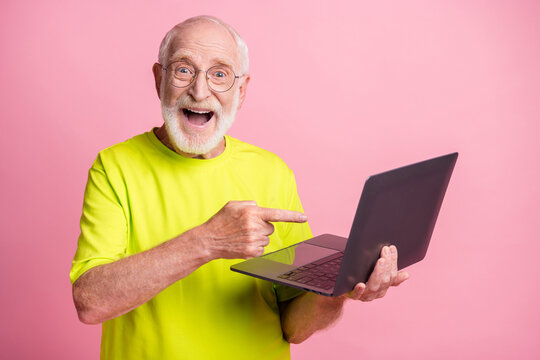 Portrait of impressed funky pensioner pointing laptop wear spectacles lime color t-shirt isolated on pastel pink color background