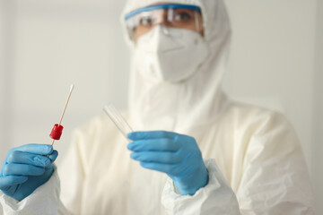 Doctor in protective suit holding test tube and cotton swab in clinic. Diagnostics covid-19 concept
