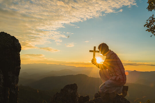 Silhouette of a young Christian man who is praying on the holy cell in the Bible and raising a cross over a Christian with a light sunset background. Christian concept