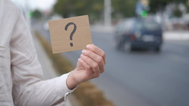 Life with questions. A view of a female hand with a question on the cardboard. A concept of unsolved problem and life with questions.