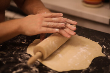 cook rolls out the dough, men's hands work with the dough, cooking dough for dumplings, cook's hands in flour