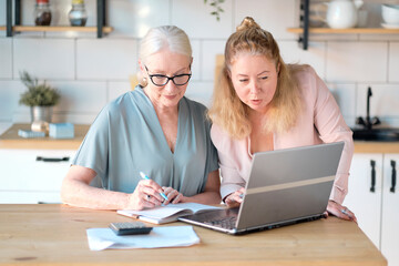 daughter helps her elderly mother figure it out online with her personal account. Woman teaching senior mother to use internet at home. Senior woman with her daughter looking at modern gadget indoors.