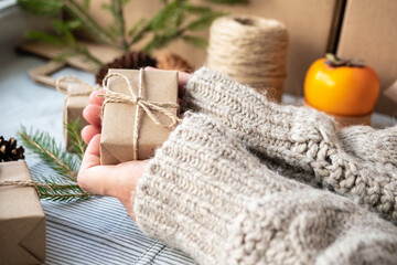 Obraz na płótnie Canvas Girl holding a gift Packed with her own hands, close-up. Christmas decoration, design of a gift box for Christmas made of natural materials. New year's atmosphere, preparation for Christmas