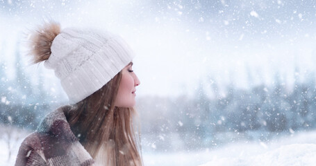 A beautiful young girl stands with closed eyes against the background of a winter forest and enjoys the first snow.
