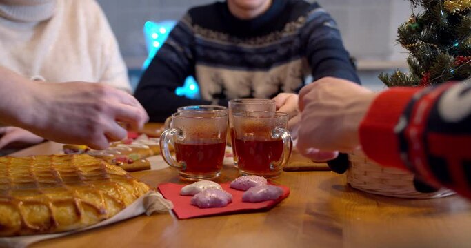 Close up shot of a friends taking tea cups from tht christmas table with sweets, ginger, pie and marshmallows. Celebrating happy new year 2021 at home during covid-19 coronavirus pandemic concept.